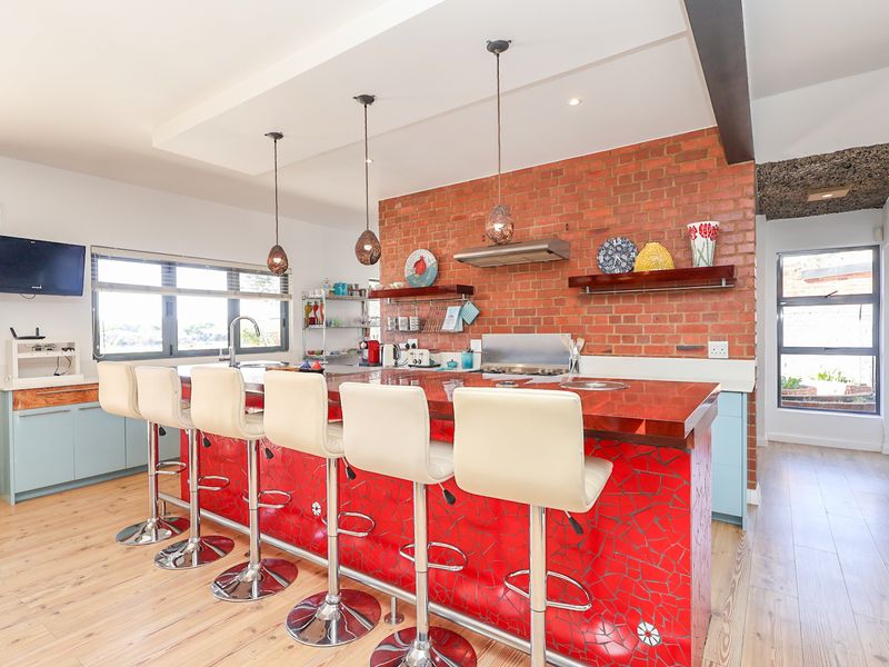 A vibrant kitchen featuring an exposed brick wall, a large island with a mosaic tile base, and modern pendant lighting over the breakfast bar.