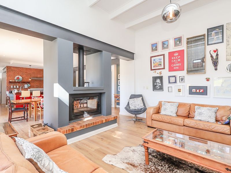 Spacious open-plan living area featuring a central built-in fireplace, exposed ceiling beams, and seamless flow into the adjacent kitchen with brick feature wall.