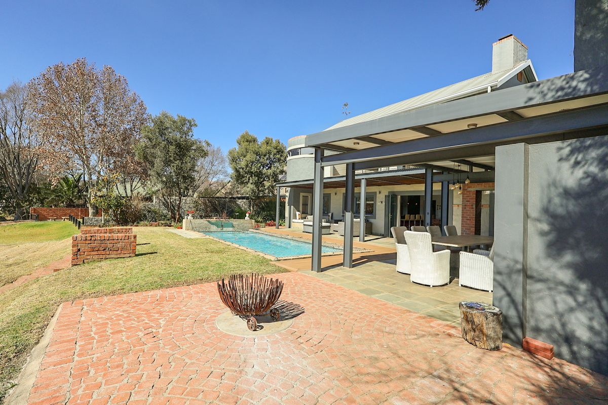 Spacious rear exterior featuring a covered patio, swimming pool with water feature, and a brick-paved outdoor entertainment area set in a landscaped garden.