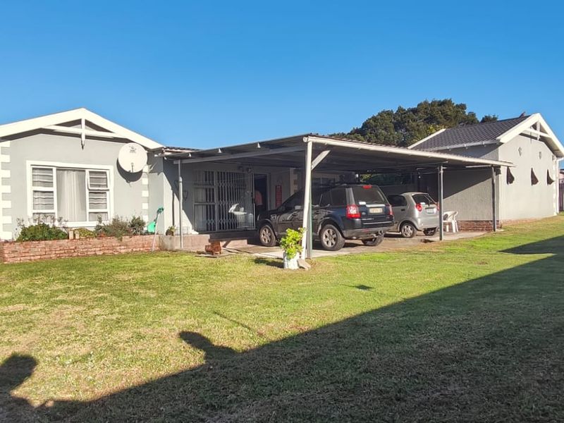 Rear view of the house featuring a spacious lawn, a covered carport area, and a brick planter box along the building facade.