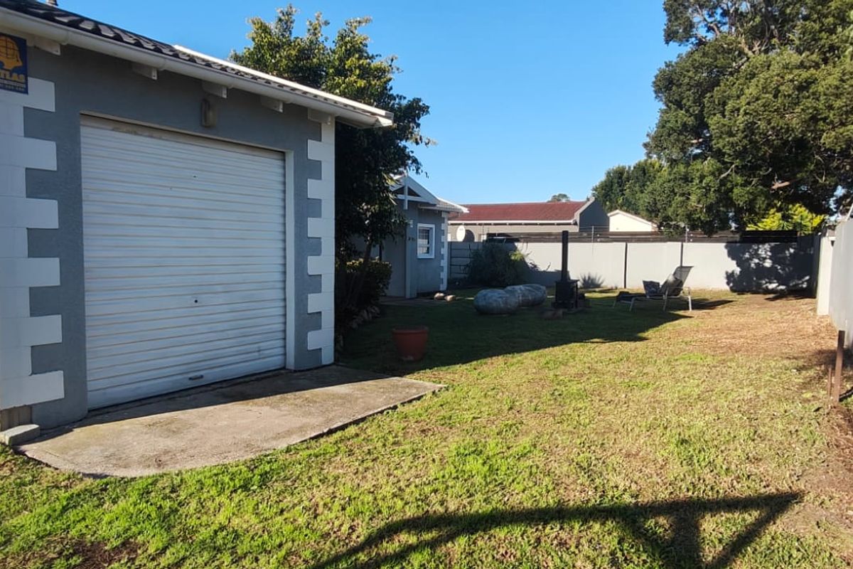 Rear garden area featuring a single garage with a roller door, concrete apron, perimeter walling with electric fencing, and a metal access gate.