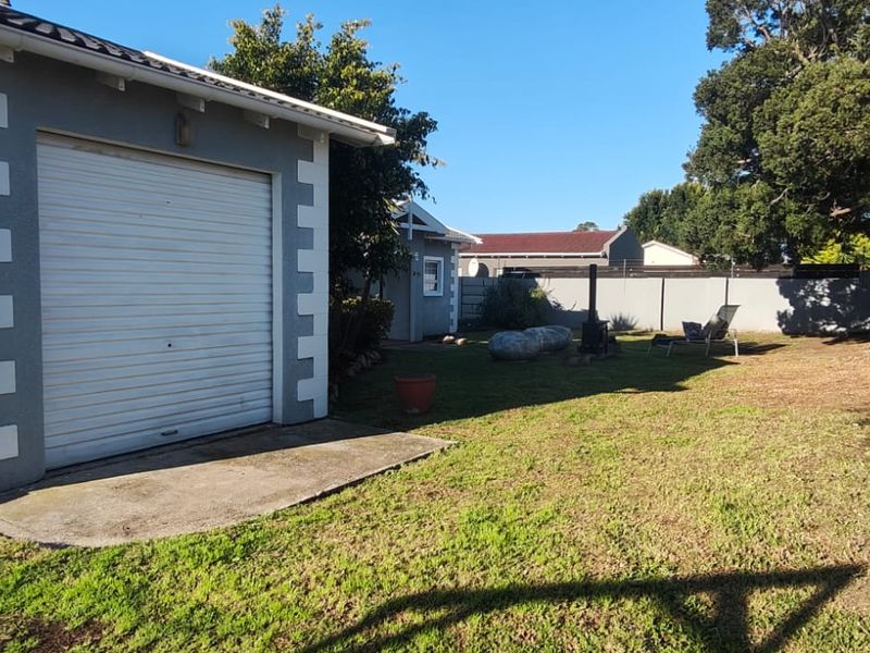 Rear garden area featuring a single garage with a roller door, concrete apron, perimeter walling with electric fencing, and a metal access gate.