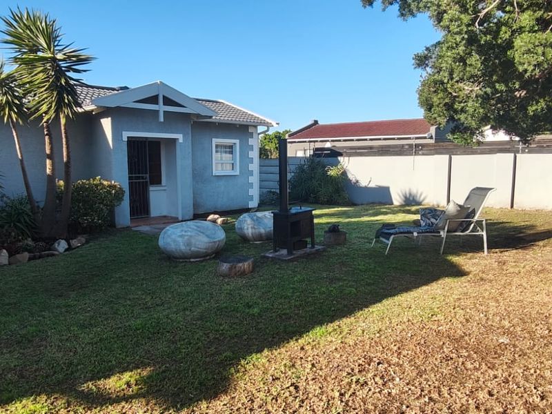 A view of the rear garden featuring a lawn area, perimeter wall, and the rear facade of the house with a tiled roof.
