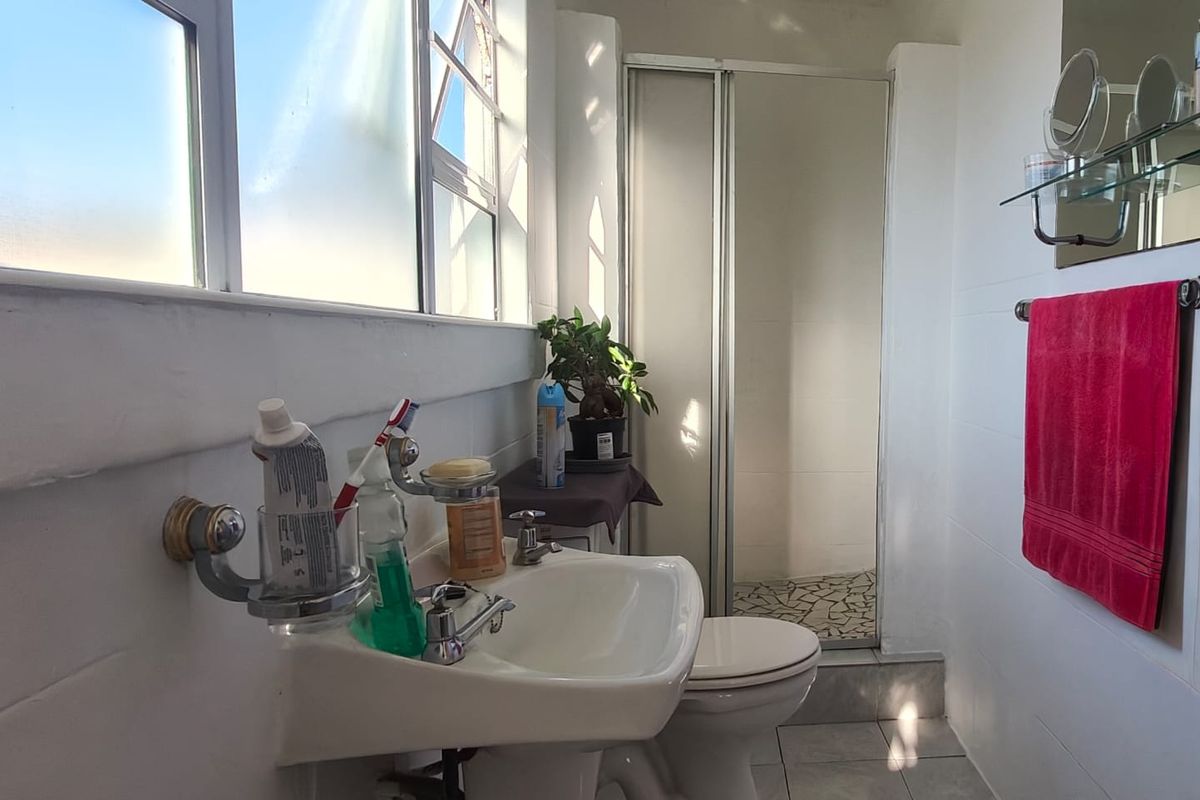 A functional bathroom featuring a pedestal basin, toilet, and a separate shower enclosure with tiled finishes and natural light.