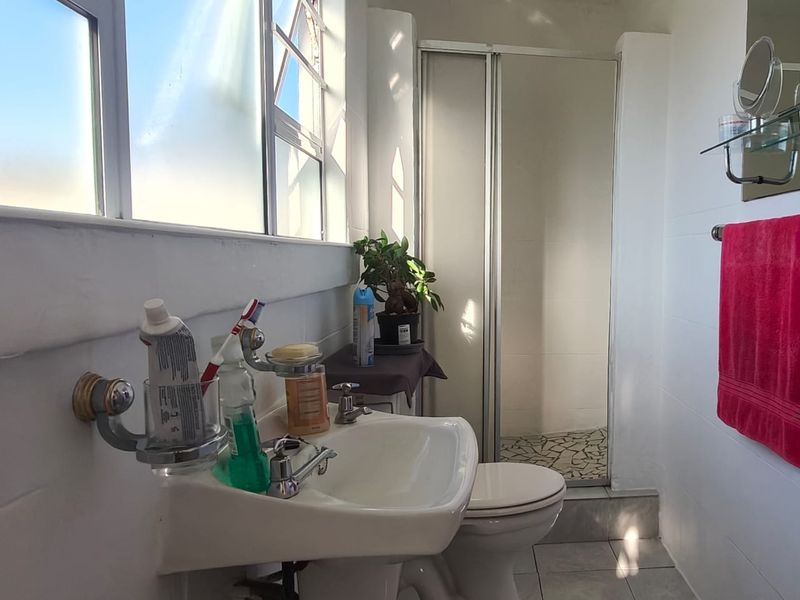 A functional bathroom featuring a pedestal basin, toilet, and a separate shower enclosure with tiled finishes and natural light.