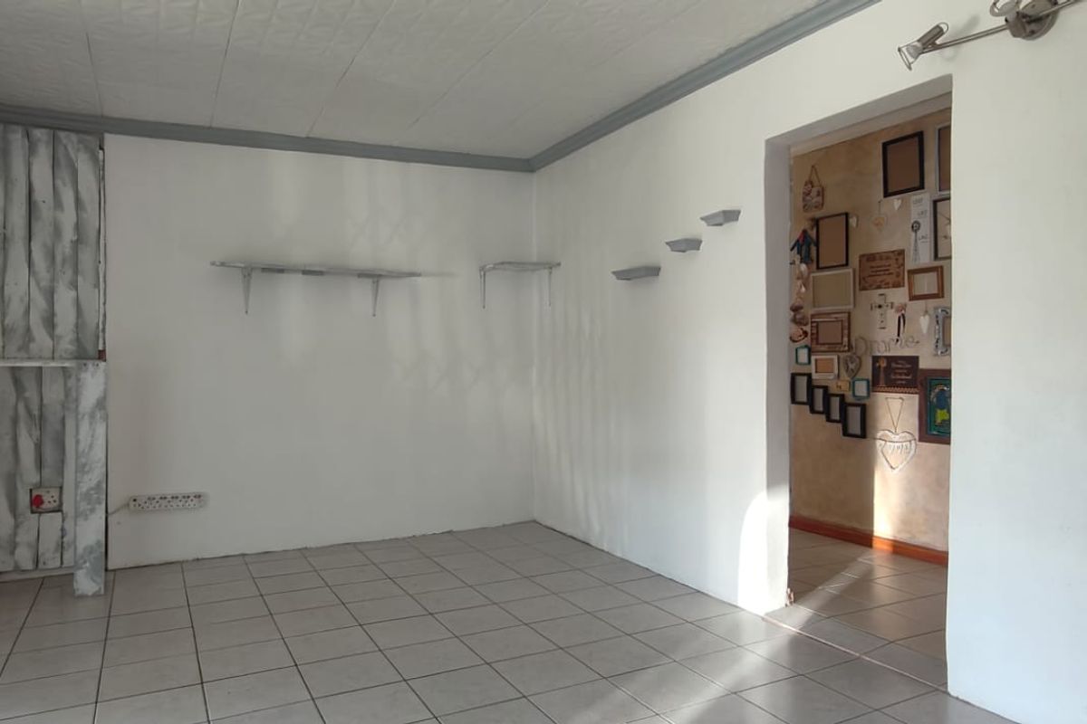 An empty living area featuring tiled flooring, ceiling tiles, and wall-mounted shelving, offering a blank canvas for renovation and interior design updates.