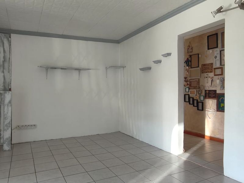An empty living area featuring tiled flooring, ceiling tiles, and wall-mounted shelving, offering a blank canvas for renovation and interior design updates.