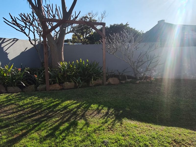 A well-maintained private garden featuring a lawn, established garden beds, a wooden pergola, and secure perimeter walling with electric fencing.