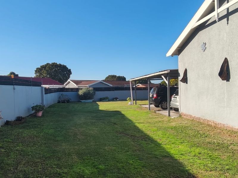 A spacious rear garden area featuring a lawn, perimeter wall with electric fencing, and a covered carport structure.