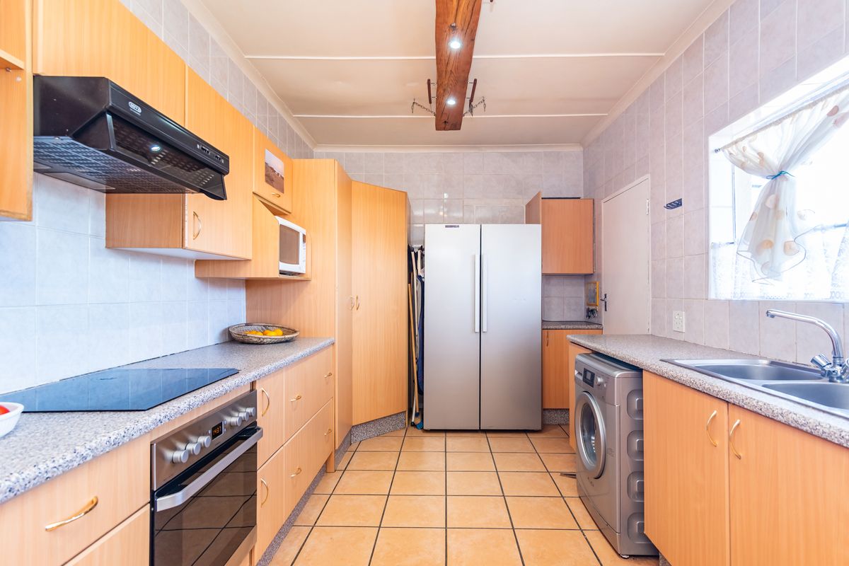 Functional kitchen featuring light wood cabinetry, laminate countertops, tiled backsplash, built-in oven with hob, and a double sink with tiled flooring.