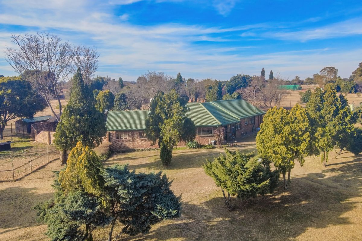 Aerial view of a facebrick small holding property featuring a green tiled roof and extensive surrounding garden with mature trees.