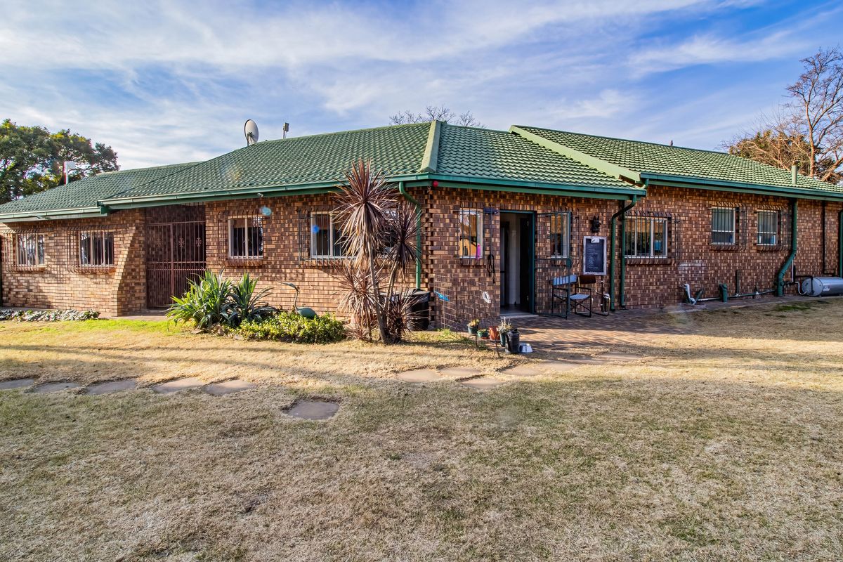 Rear view of a facebrick small holding dwelling featuring a pitched tiled roof, security bars on windows, and a paved patio area.