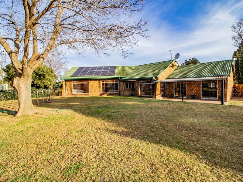 Rear view of a brick-faced small holding featuring a tiled roof with solar panels, security bars on windows, and a covered patio area.
