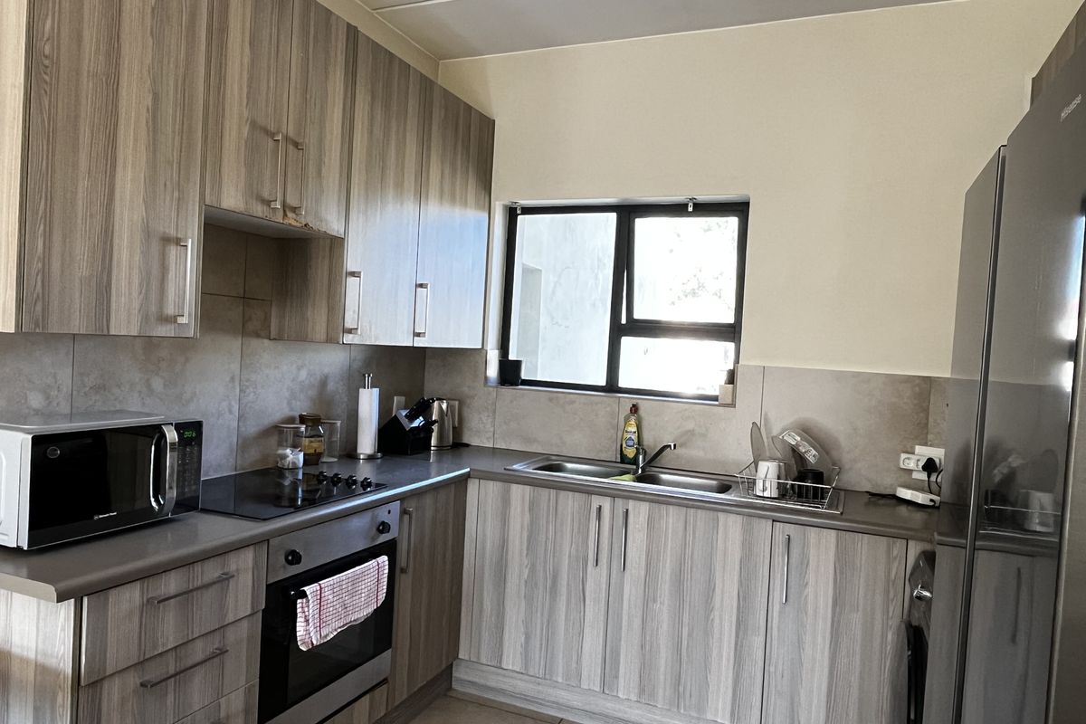 A functional kitchen featuring wood-look laminate cabinetry, stone-effect countertops, a built-in oven with electric hob, and a stainless steel double sink.