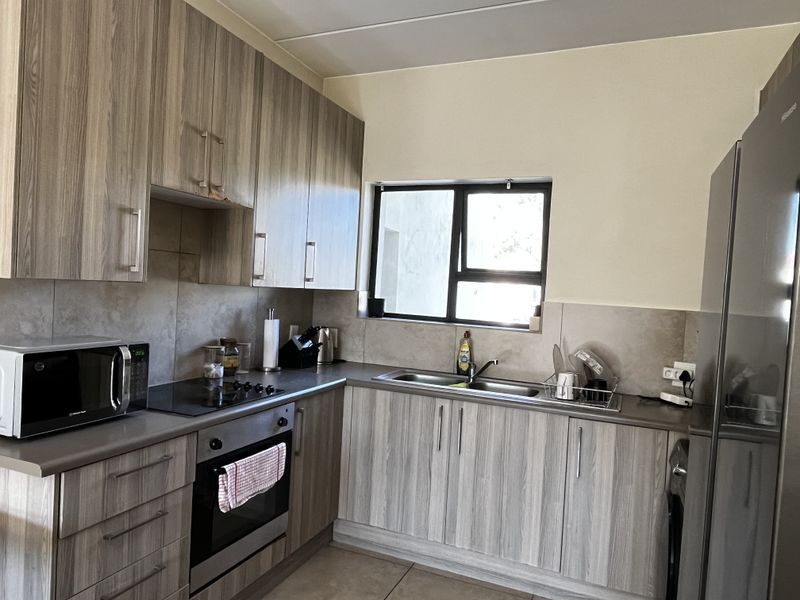 A functional kitchen featuring wood-look laminate cabinetry, stone-effect countertops, a built-in oven with electric hob, and a stainless steel double sink.