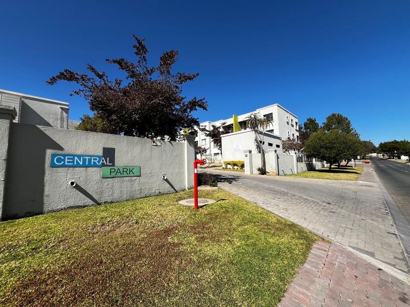 Street view of the Central Park residential complex entrance, featuring a paved driveway, boundary wall, and clear signage.