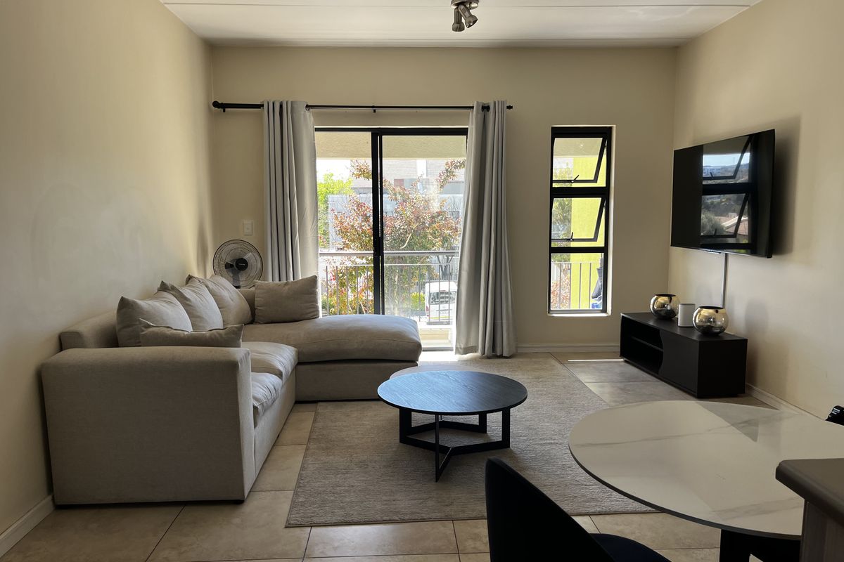 A well-lit living room featuring tiled flooring, a sliding glass door leading to a balcony, and a large window providing natural light.