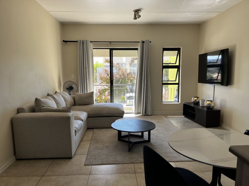 A well-lit living room featuring tiled flooring, a sliding glass door leading to a balcony, and a large window providing natural light.