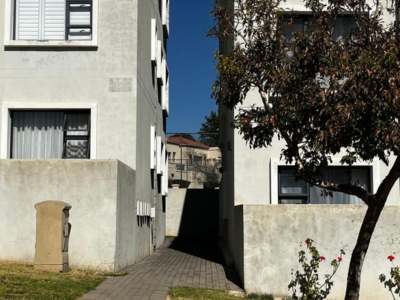 Exterior view of the apartment complex showing a paved walkway between two building blocks with established landscaping.