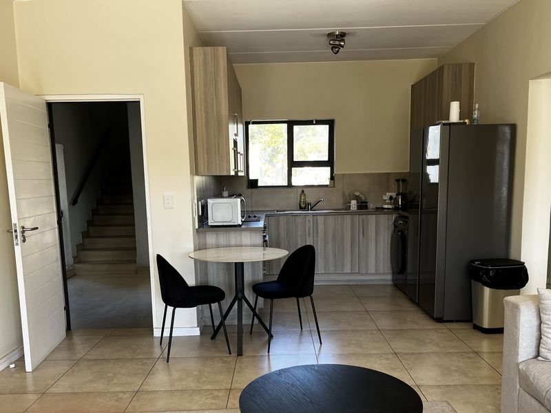 Open plan kitchen and living area featuring modern wood-look cabinetry, tiled flooring, and direct access to the hallway.