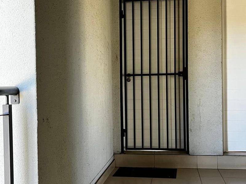A covered entrance area featuring tiled flooring, a black security gate, and a metal balustrade.