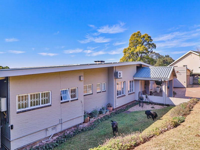 Rear view of the property featuring a brick exterior, metal roofing, a covered patio area, and a paved driveway.