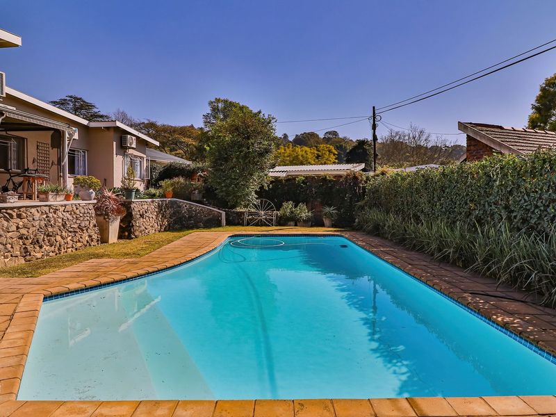 A well-maintained swimming pool area featuring a stone retaining wall, paved surround, and a covered patio area adjacent to the main house.
