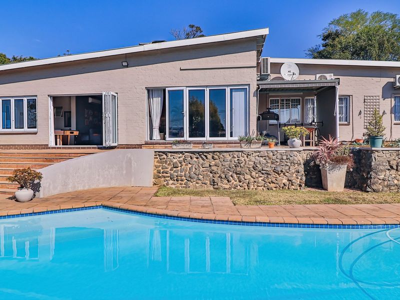 Rear elevation featuring a swimming pool, stone retaining wall, tiled patio area, and bi-fold doors providing seamless indoor-outdoor flow.