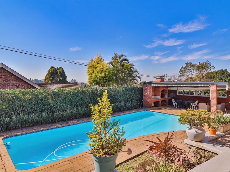 Outdoor entertainment area featuring a swimming pool and a covered patio with a built-in brick braai, perfect for summer gatherings.