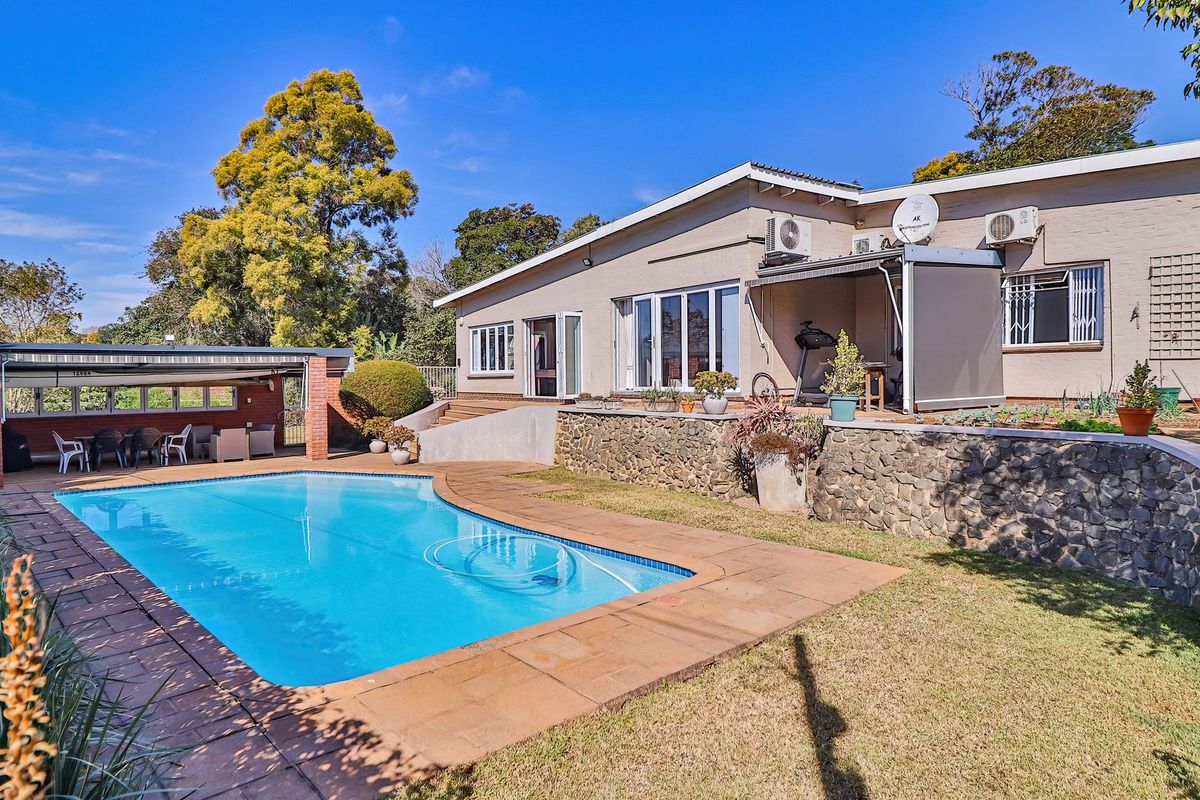 Rear exterior view featuring a swimming pool, stone retaining wall, and a covered patio area adjacent to the main house structure.