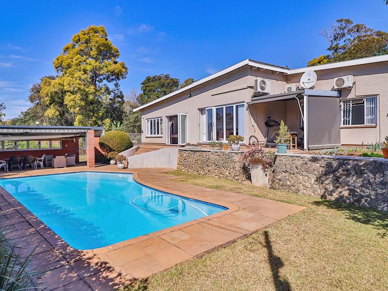 Rear exterior view featuring a swimming pool, stone retaining wall, and a covered patio area adjacent to the main house structure.