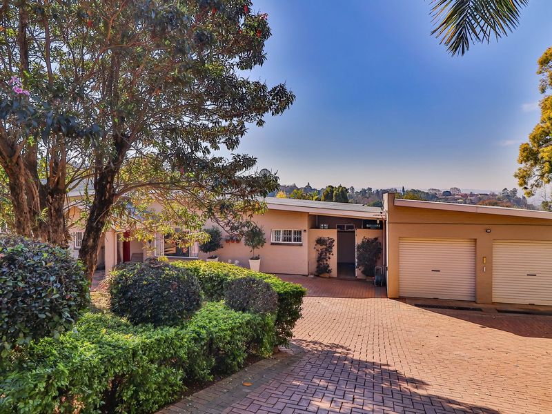 Front elevation of a residential property featuring a double garage, brick paved driveway, and established landscaped garden.