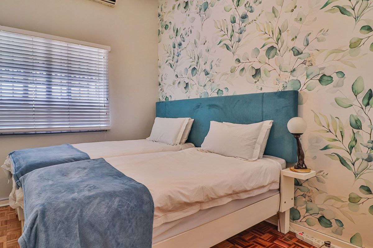 A well-maintained bedroom featuring parquet flooring, a decorative botanical feature wall, and venetian blinds for light control.