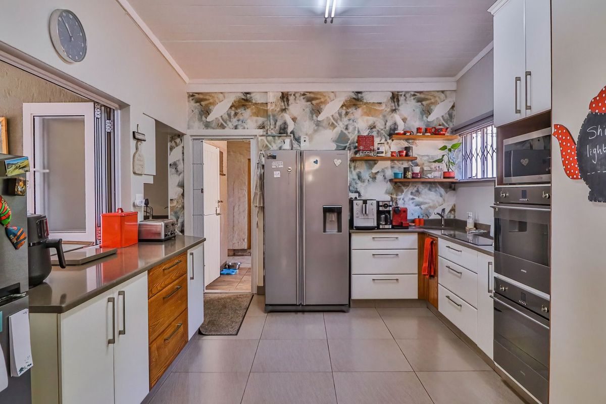 A functional kitchen featuring modern white and wood-toned cabinetry, stone countertops, built-in appliances, and decorative wallpaper accents.