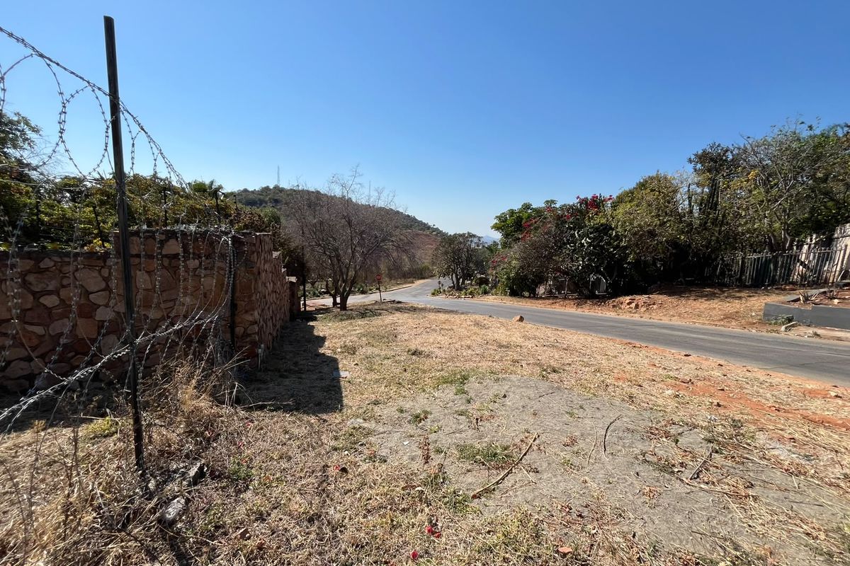 A street-level view of the property frontage, featuring a stone boundary wall with barbed wire fencing along an asphalt road.