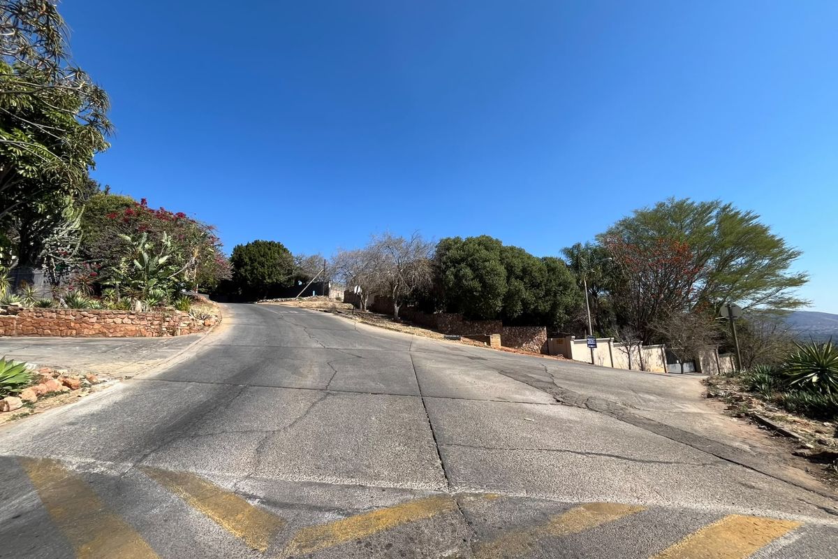 A view of the paved street approach leading up to the residential property, featuring mature landscaping and stone retaining walls.