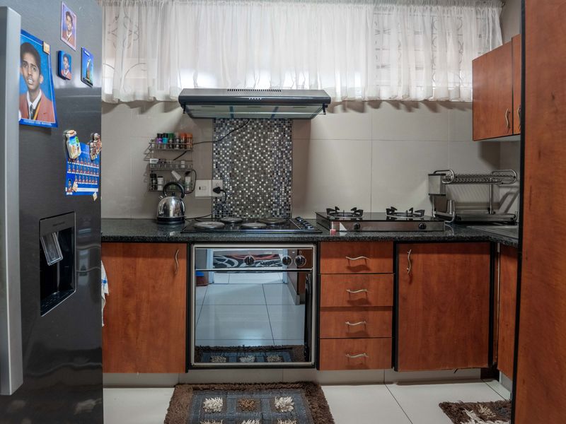 A functional kitchen featuring wood-finish cabinetry, granite countertops, a mosaic tile backsplash, and a combination of electric and gas hobs with an extractor fan.
