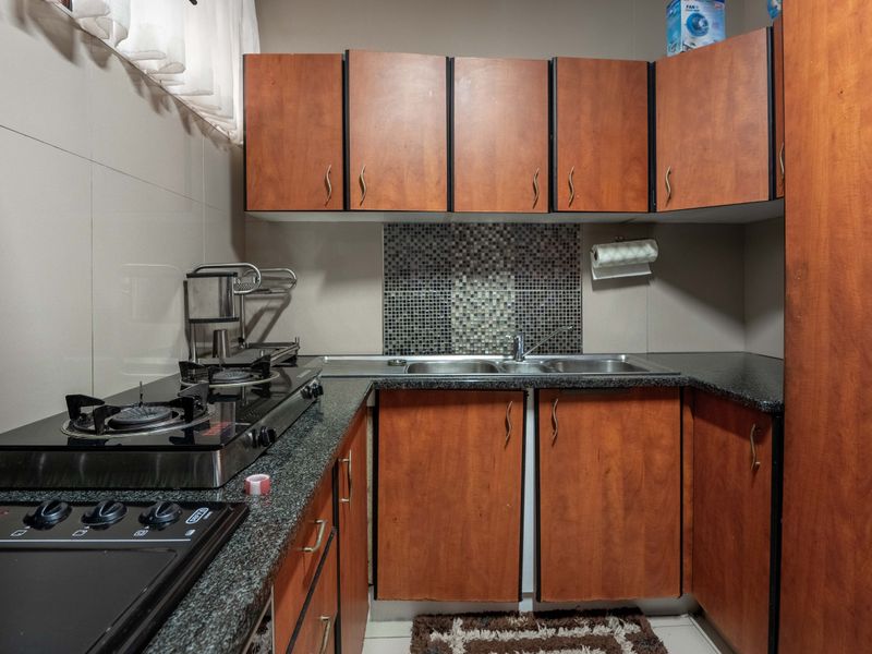 Compact kitchen featuring wooden cabinetry, granite countertops, a gas hob, and a mosaic tile backsplash, offering a functional workspace.