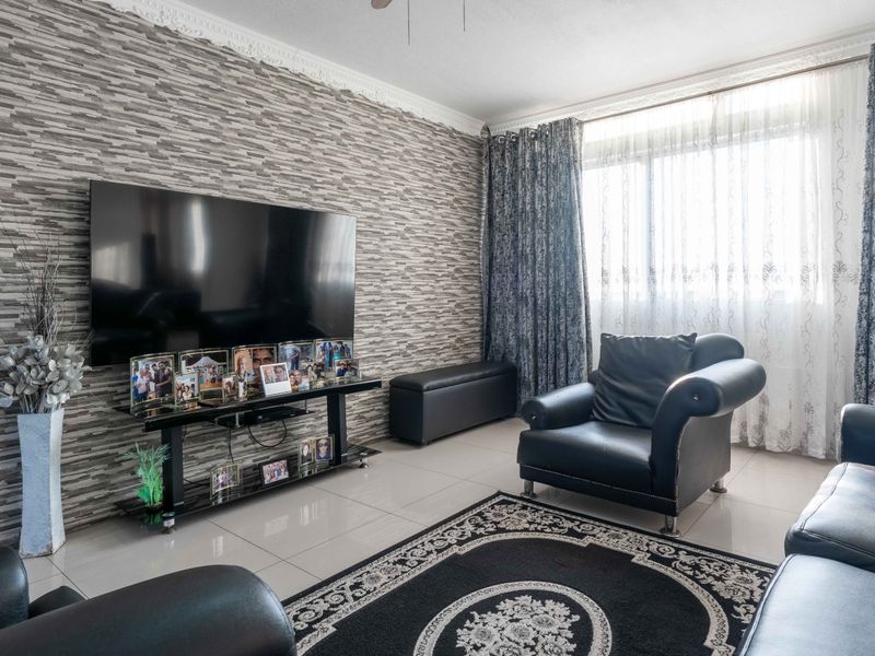 A living room featuring tiled flooring, a textured feature wall, and decorative ceiling cornicing, providing a neutral base for interior updates.