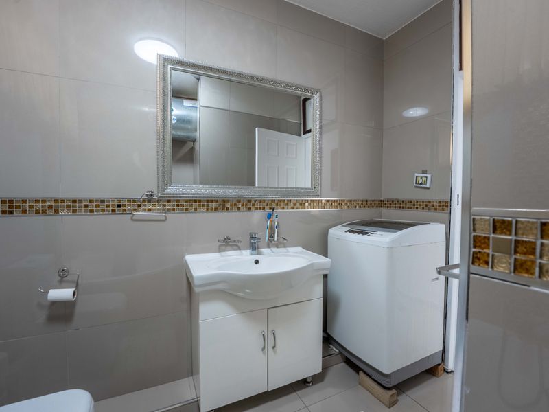 A functional bathroom featuring tiled walls with a mosaic accent, a vanity cabinet with a basin, and space for laundry appliances.