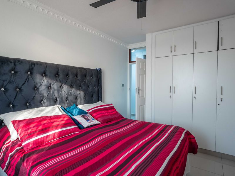 A well-maintained bedroom featuring built-in white cupboards, a ceiling fan, and decorative cornice detailing, finished with clean tiled flooring.