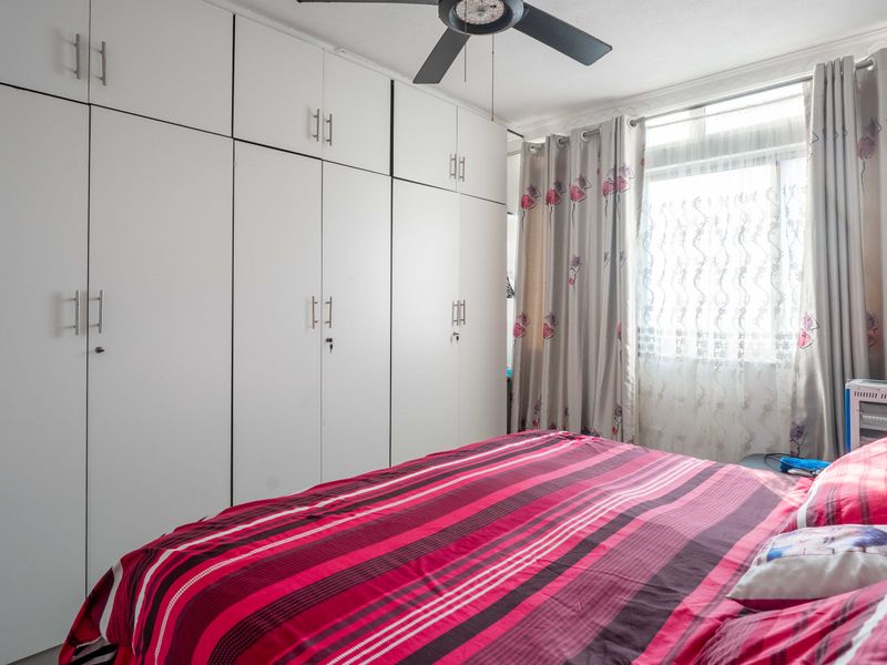A well-maintained bedroom featuring extensive floor-to-ceiling built-in cupboards and a ceiling fan, providing ample storage and ventilation.