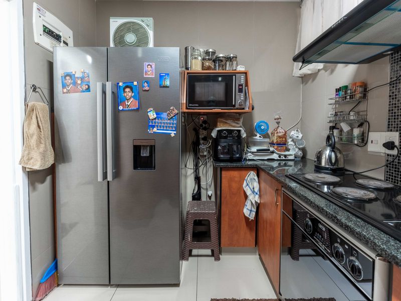 A functional kitchen featuring granite countertops, built-in cabinetry, an electric hob with extractor fan, and tiled finishes throughout.