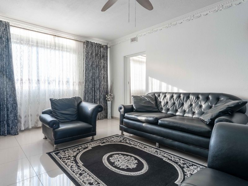 A well-lit living room featuring tiled flooring, decorative ceiling cornices, and a ceiling fan, providing a comfortable and functional living space.