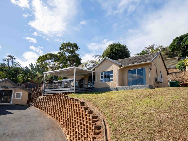 Rear view of the property featuring a covered patio, sliding glass doors, and a tiered lawn with a brick retaining wall.