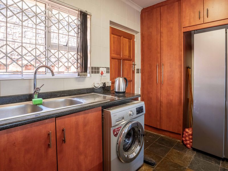 Functional laundry area featuring built-in wooden cabinetry, stone countertops, a double stainless steel sink, and durable slate flooring.