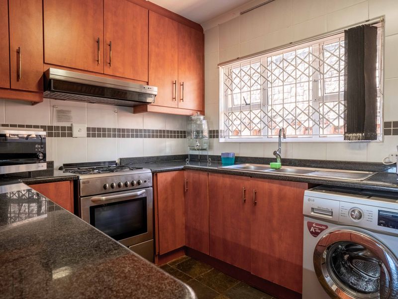 A functional kitchen featuring wood-finish cabinetry, granite countertops, a stainless steel gas stove, and a double bowl sink with tiled backsplash.