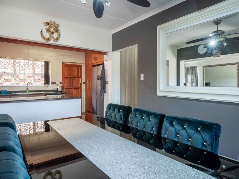 Open-plan dining area adjacent to a functional kitchen featuring granite countertops, built-in cabinetry, and a ceiling fan.