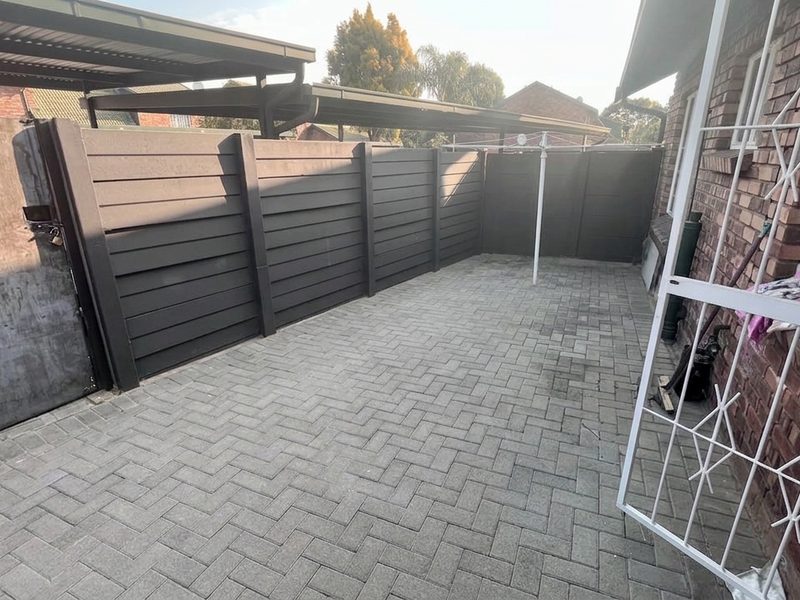 A paved rear courtyard area featuring perimeter fencing, a security gate, and access to a covered carport structure.
