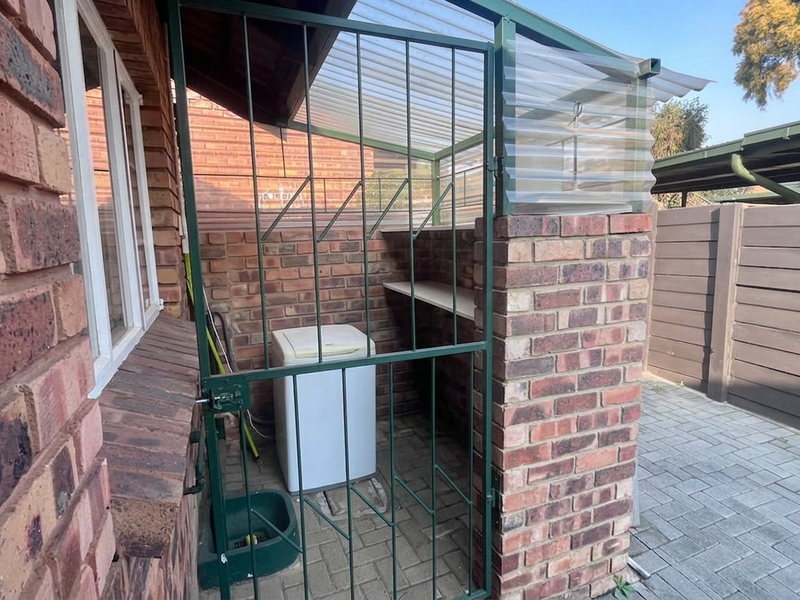 An outdoor utility area featuring brick walls, a corrugated roof, and a secure metal gate, providing a functional space for storage or laundry tasks.